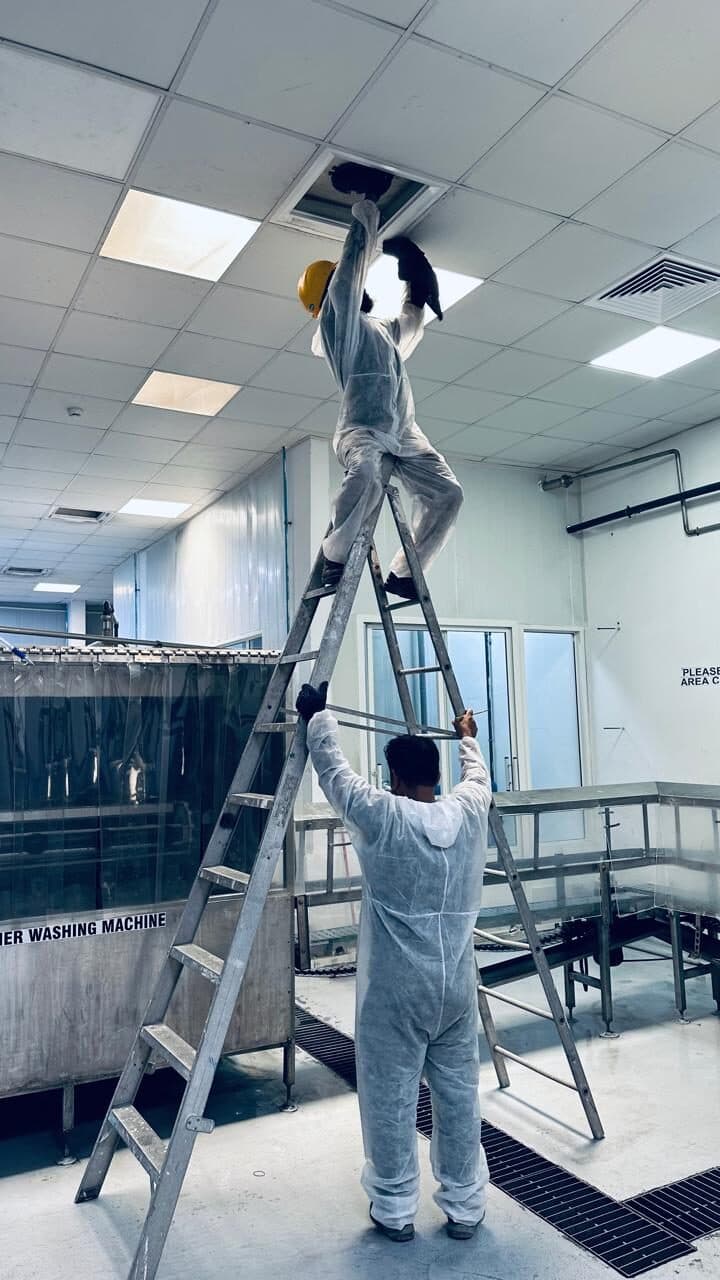 HoodEx technician on a ladder opening a ceiling duct access panel for cleaning in a food-production facility