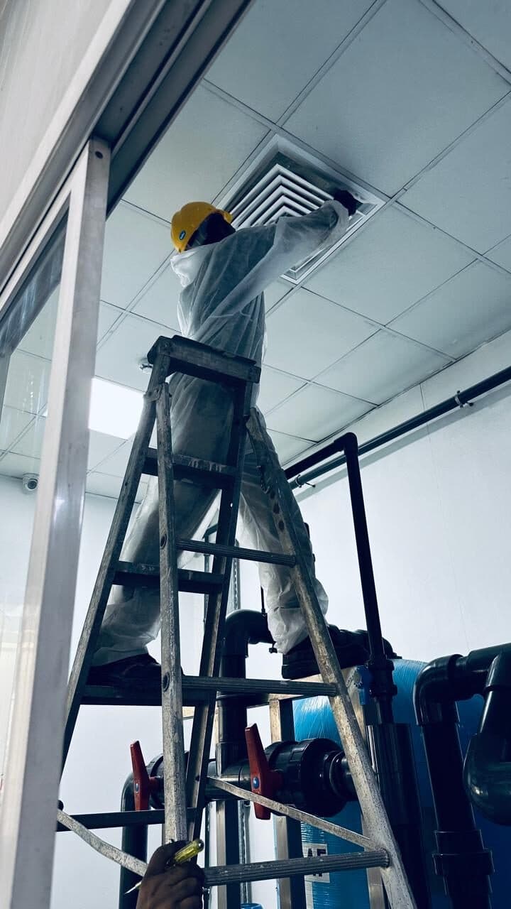 HoodEx technician in protective suit and hard hat cleaning a ceiling ventilation diffuser