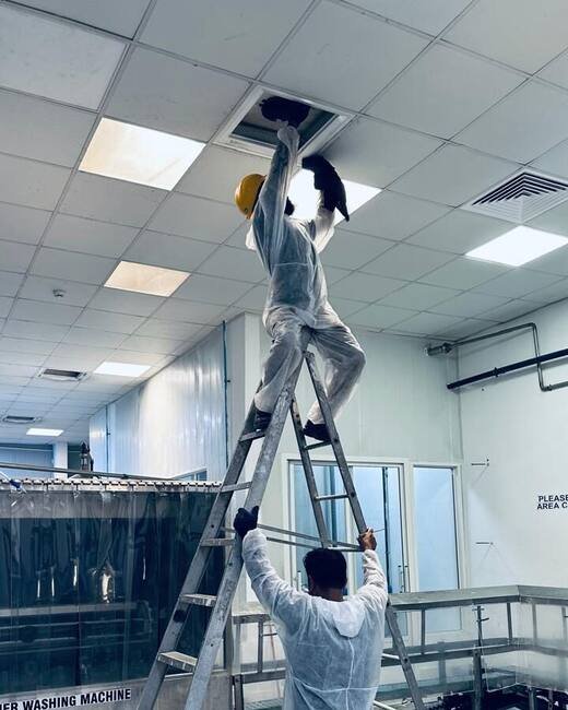 HoodEx technician on a ladder opening a ceiling duct access panel for cleaning in a food-production facility